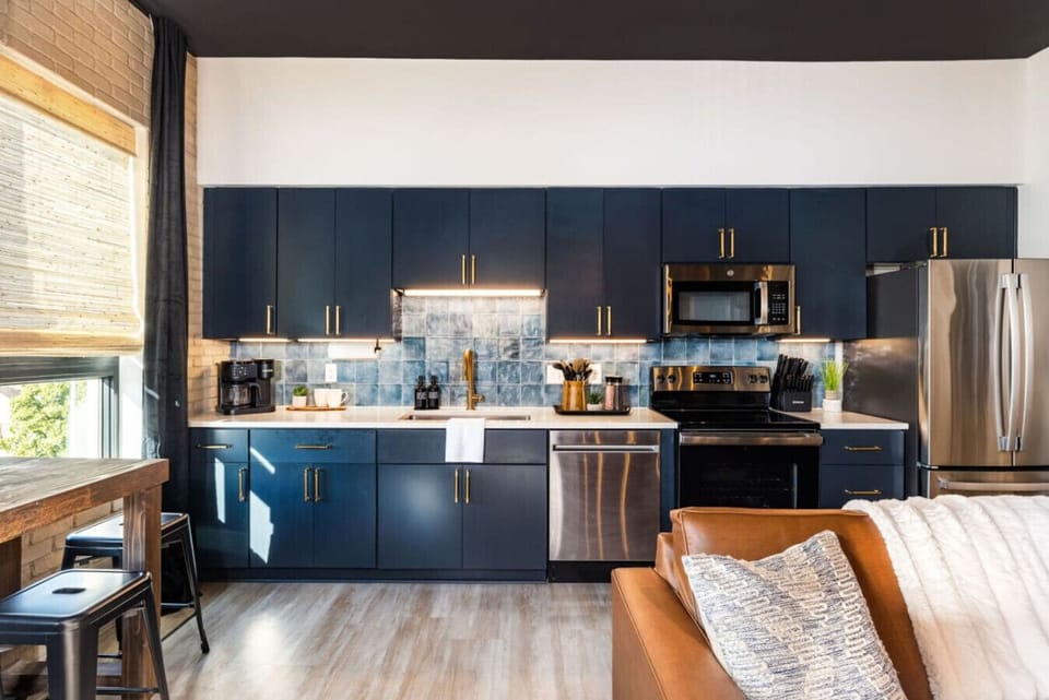 A bold navy kitchen with gold hardware and a teal tile backsplash.