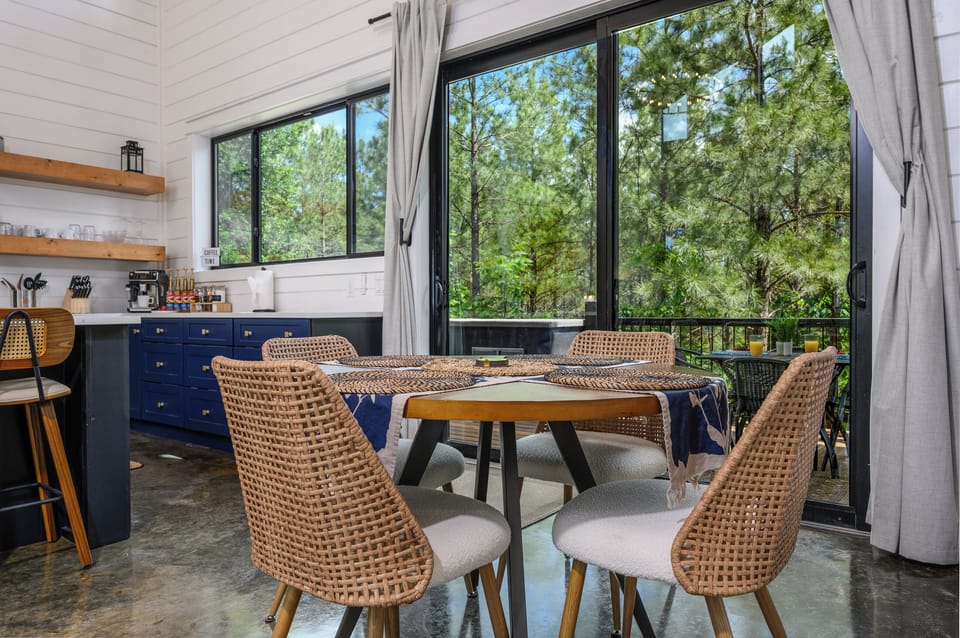 Dining space features woven seating, forest views, and direct deck access.