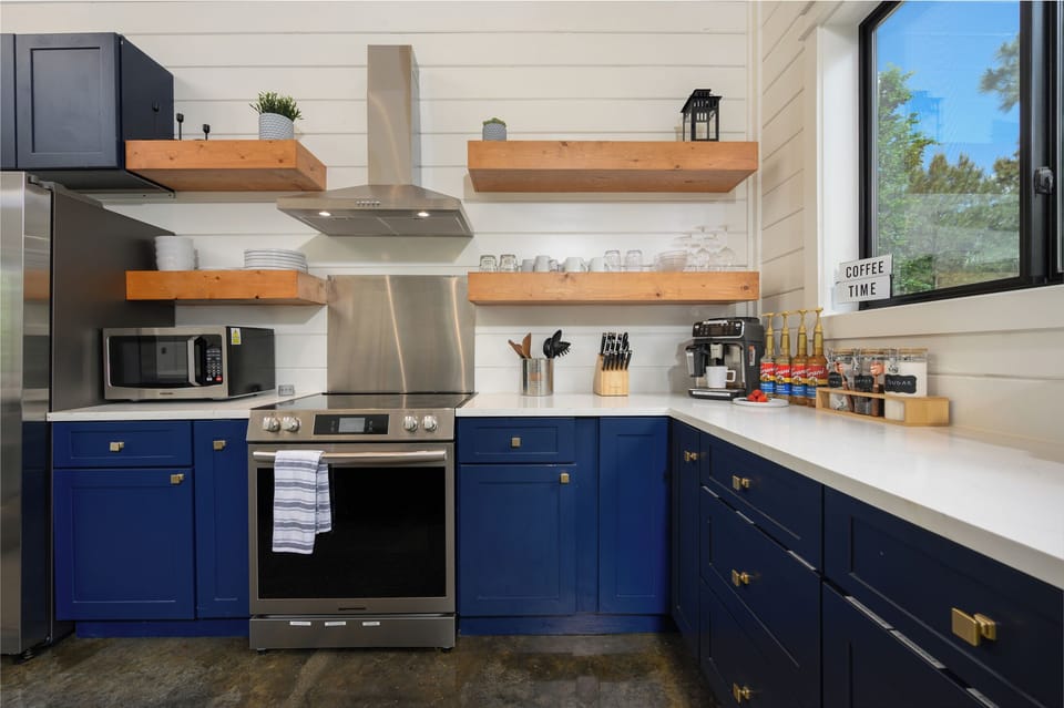 Kitchen features bold navy cabinets, open shelving, and a full coffee station.