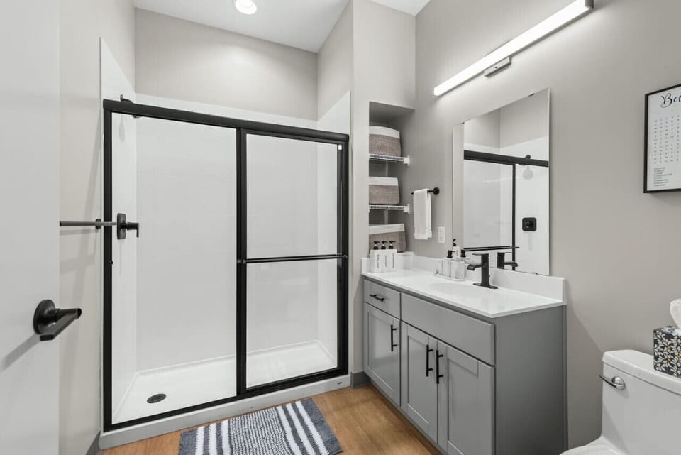 Full bathroom with glass-enclosed shower, modern vanity, mirror, and guest toiletries.