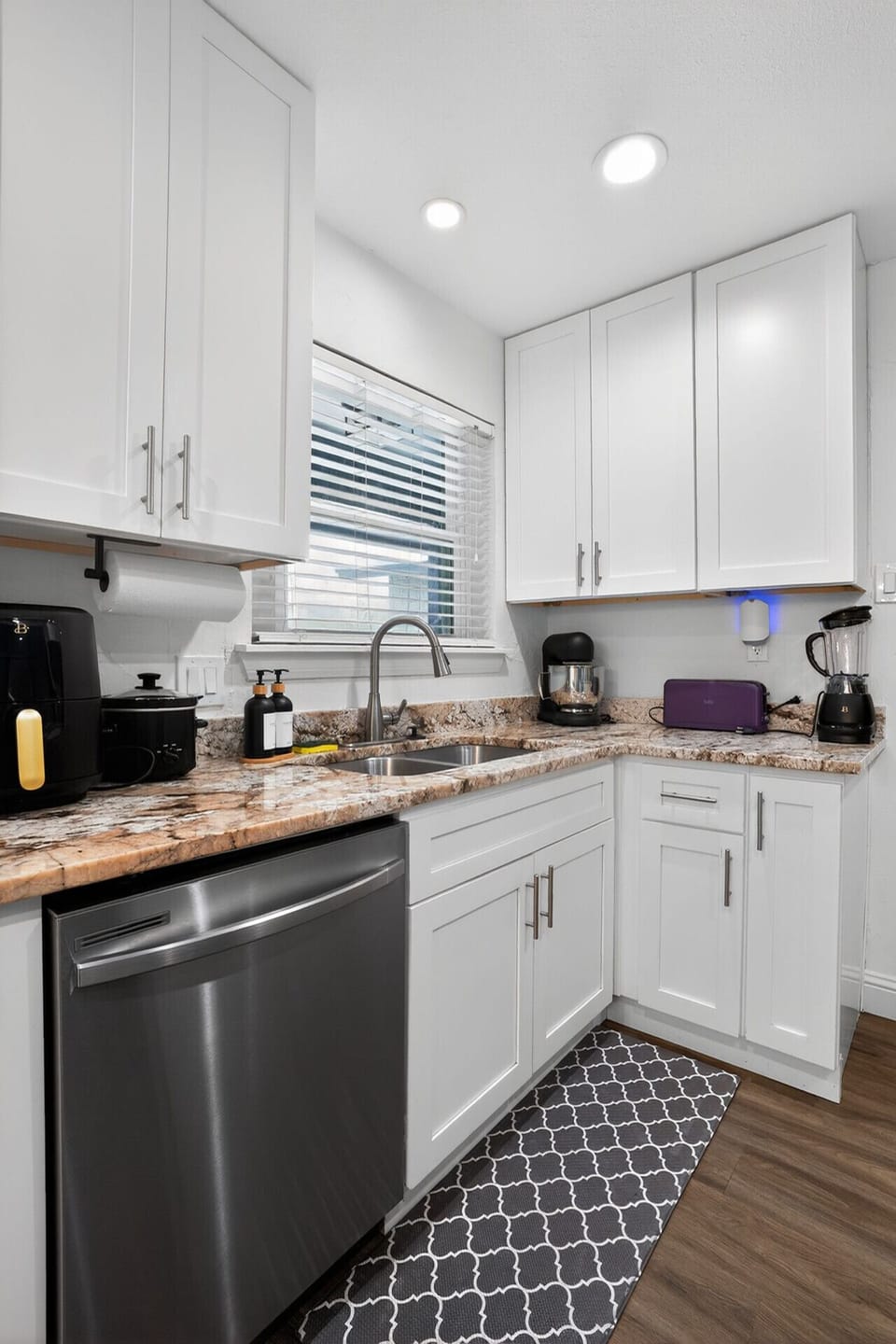 Fully equipped kitchen with sleek white shaker cabinets, stunning granite countertops, stainless steel dishwasher, deep undermount sink, and all small appliances — coffee maker, blender, air fryer, and more provided for your stay.