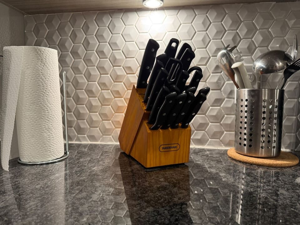 - Complete knife set and cooking utensils on granite counter - Modern kitchen essentials for home style meal prep - Well equipped apartment kitchen with ample prep space