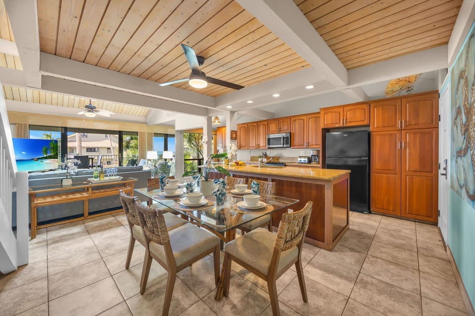 Glass-topped dining waits beneath the fan, kitchen and table flowing together in one open space.