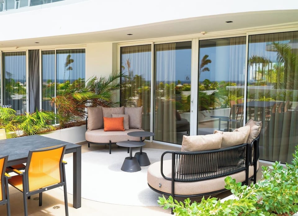 Seamless indoor-outdoor luxury—this expansive patio flows with sleek modern furnishings, lush tropical landscaping, and floor-to-ceiling glass doors that create the perfect alfresco entertaining space with stunning ocean views.