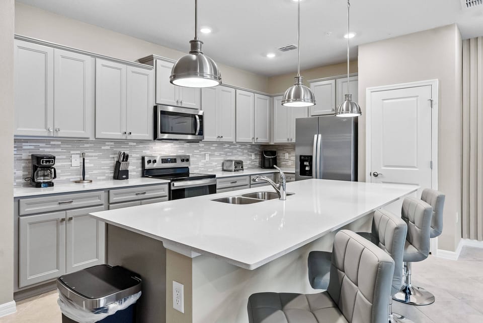 This stylish kitchen boasts sleek white cabinetry and a spacious island with modern seating, perfect for casual dining or morning coffee. Stainless steel appliances and an elegant backsplash elevate your culinary experience.