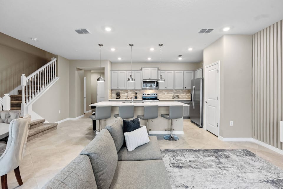 Experience a stylish living area that seamlessly connects to a gourmet kitchen with modern stainless steel appliances and a spacious island with chic bar stools, all enhanced by soft neutral tones for a cozy and inviting.