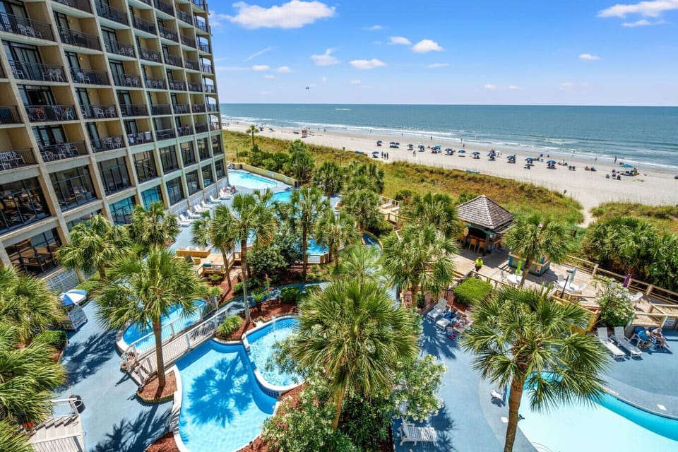 Stunning balcony view overlooking sparkling pools, relaxing hot tubs, a lively beach bar, glowing fountains, and the illuminated North Myrtle Beach shoreline.  Perfect for capturing the resort’s vibrant nightlife and coastal charm.