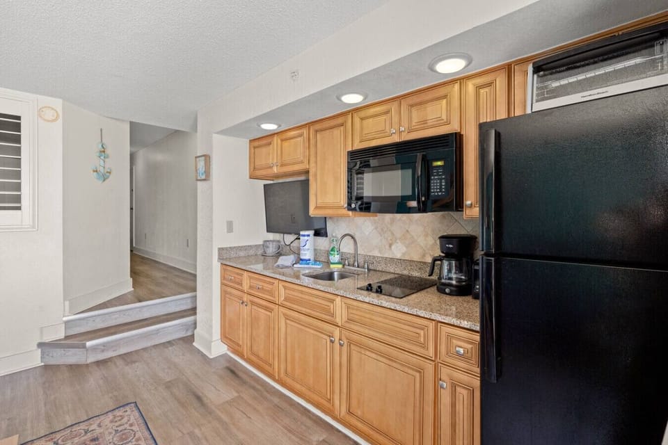 Ideal for preparing family meals on your beach getaway, this coastal-themed kitchen features a refrigerator, microwave, stovetop burners, sink, Smart TV, and ample cabinet storage; blending style, function, and ocean-inspired charm.