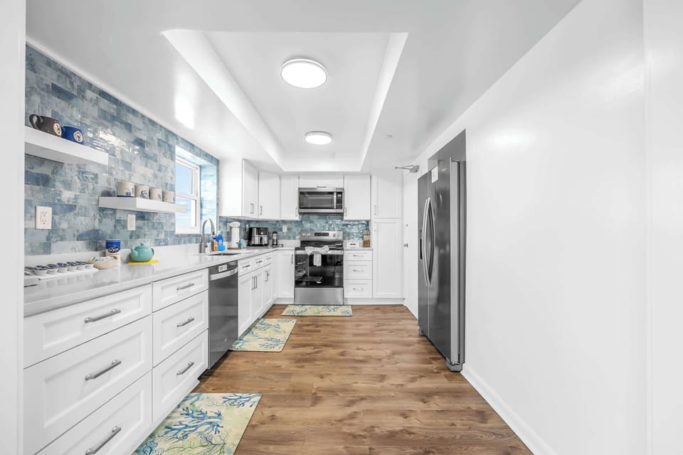 Modern kitchen with white cabinetry, blue tile backsplash, and stainless steel appliances.
