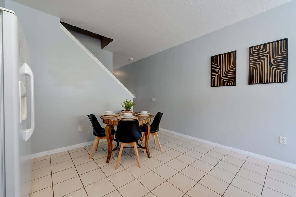 Dining area with a round wooden table and modern black chairs under the staircase.