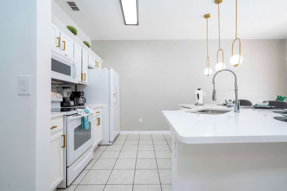 Whip up culinary delights in this bright, modern kitchen! Features sleek white cabinetry, quartz island with spring faucet, gold-accent pendant lights, and seating at the island-perfect for casual breakfasts or evening cocktails.