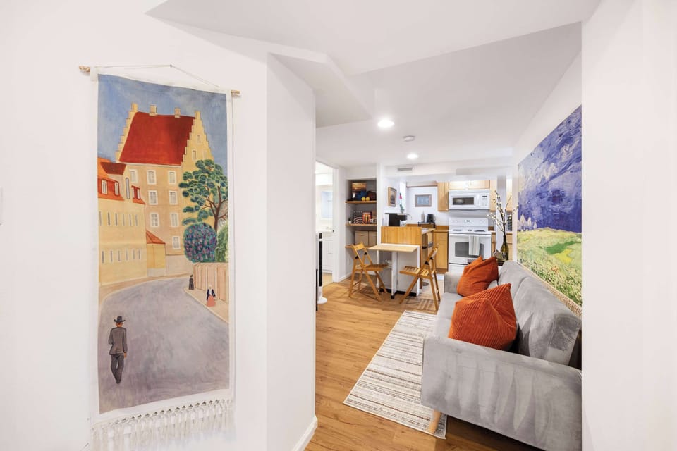 Art meets modern efficiency: the Decorative painting in oil tone watches over a compact kitchen-dining area where orange sofa cushions mirror the warmth of wooden table settings.