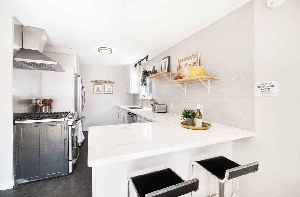 Stainless steel appliances and marble countertops keep this white kitchen sleek,while open shelving displays decor and a ‘NO SMOKING’ sign hints at shared household rules.