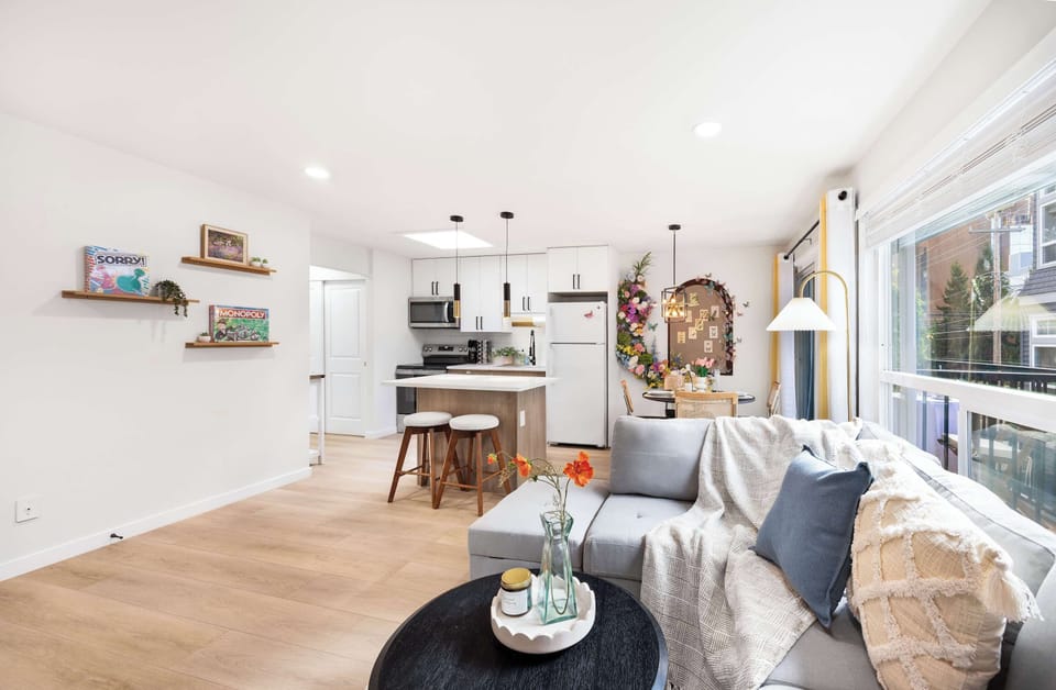 A modern and bright living area featuring a comfortable seating arrangement, sleek kitchen with island seating, and a colorful floral area