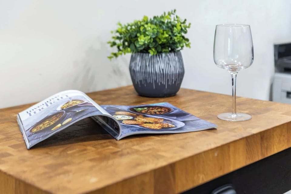 Cozy countertop moment with a recipe magazine, wine glass, and potted plant. A stylish nook perfect for culinary inspiration and quiet relaxation.