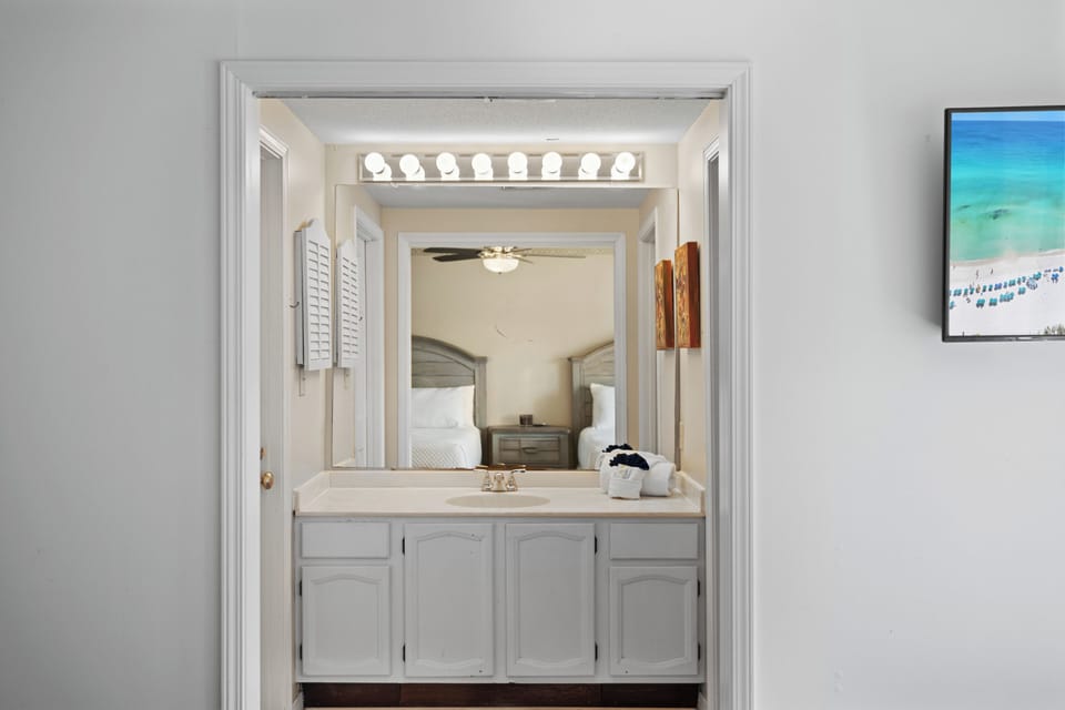 Guest ensuite vanity area with wide countertop, large mirror, bright Hollywood-style lighting, and white cabinetry. Clean and functional, with direct access to the bedroom.