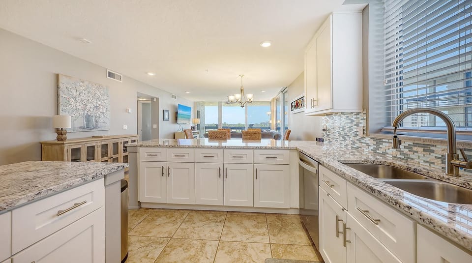 White cabinets and granite counters frame the galley kitchen with mosaic tile backsplash and stainless steel sink.