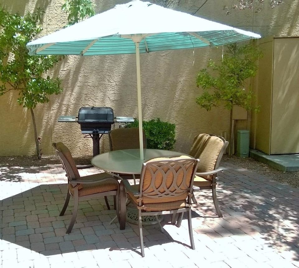 This cozy outdoor dining space features a shaded table and grill, ideal for enjoying delicious meals in the tranquil Sedona sun amidst the greenery.