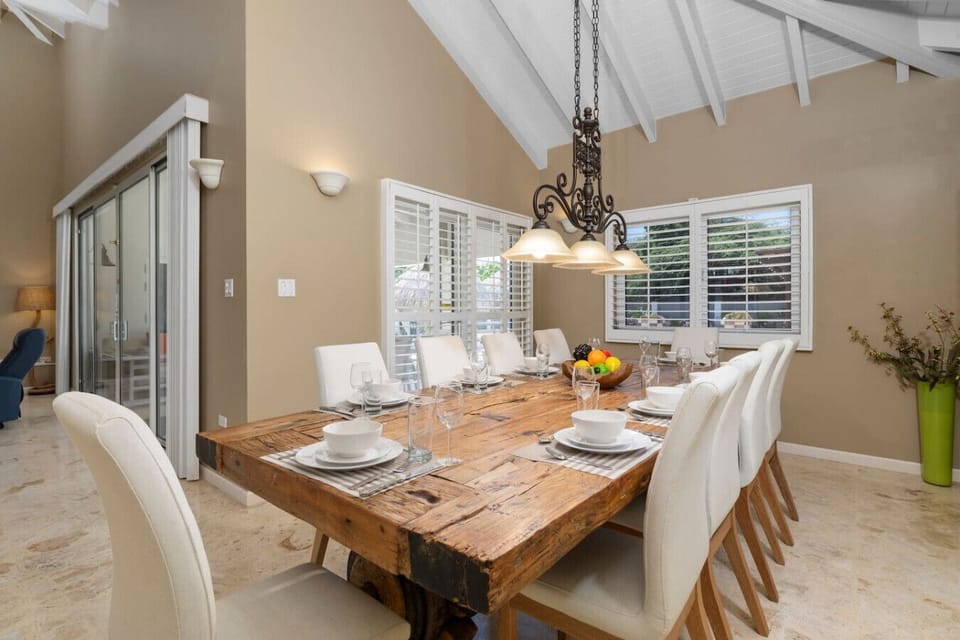 This charming dining area features a rustic wooden table with seating for eight, elegant white chairs, and a stylish chandelier. Large windows let in natural light, creating a bright and inviting space, perfect for family meals and gatherings.