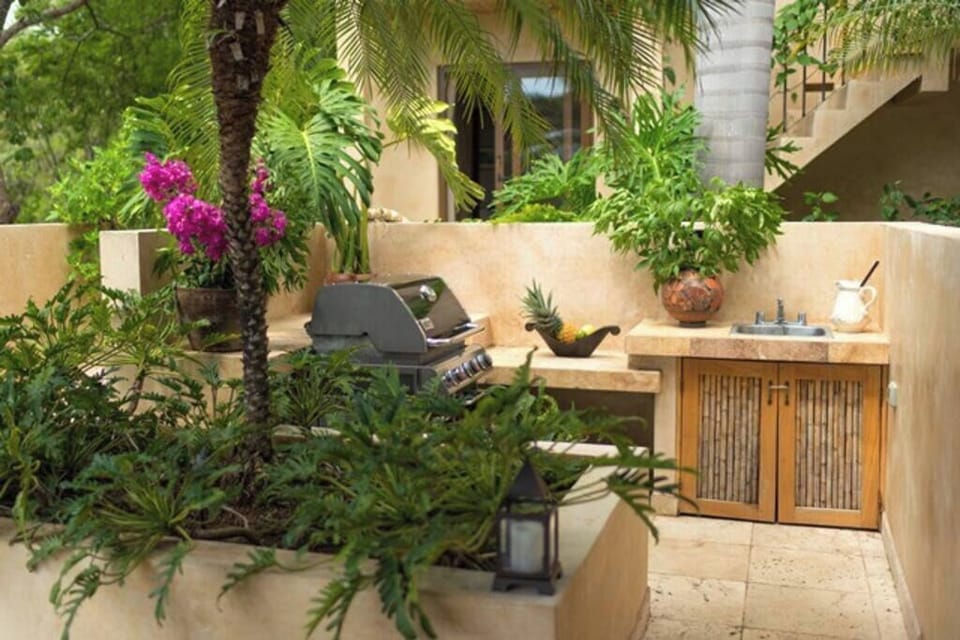 Spacious outdoor BBQ area with a large sink, surrounded by lush tropical gardens — perfect for family gatherings and entertaining during your Tamarindo vacation.
