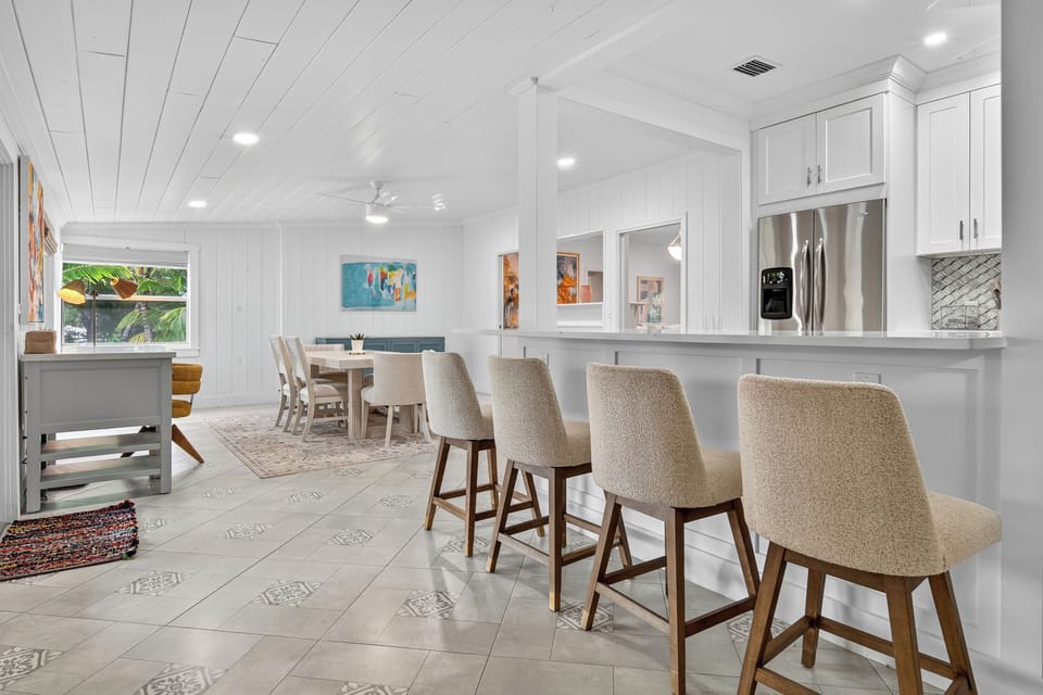 Experience our open-concept living. A spacious dining area flows into a fully equipped kitchen, perfect for shared meals. Large windows offer serene views, complemented by a crisp white shiplap ceiling for a fresh ambiance.