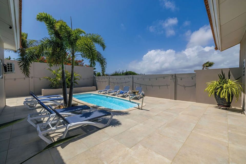 Your private oasis awaits—lounge by the sparkling pool under swaying palms, soak up the sun on a comfy chair, and let the warm breeze wash over you in this peaceful retreat.