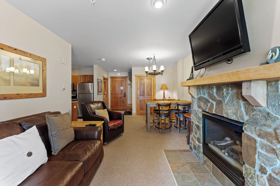 Relax in your spacious living area with crackling stone fireplace, comfortable leather seating, and mountain lodge charm that makes every evening feel special.