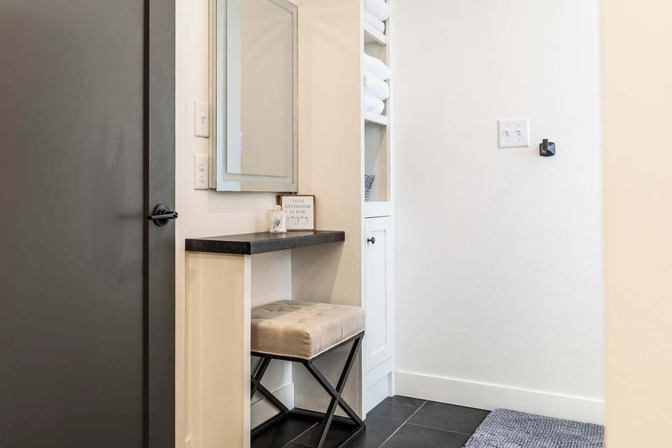 This bathroom includes a stylish makeup station with a table, bench seating, and mirror. A convenient and comfortable spot to get ready, offering extra space beyond the standard bathroom setup.
