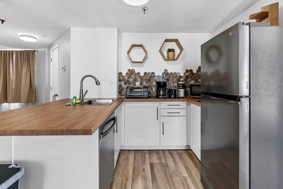 This bright kitchen boasts a warm wood countertop and sleek stainless steel appliances for your culinary adventures. Unique hexagonal decor adds charm, while soft lighting creates an inviting atmosphere for all your cooking needs.