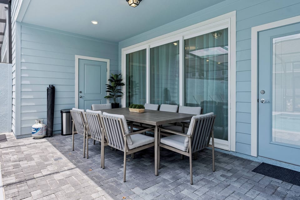Enjoy al fresco dining on our spacious patio, featuring a sleek wooden table and comfortable modern chairs. With soft blue walls and large windows, this bright area is perfect for relaxing moments.