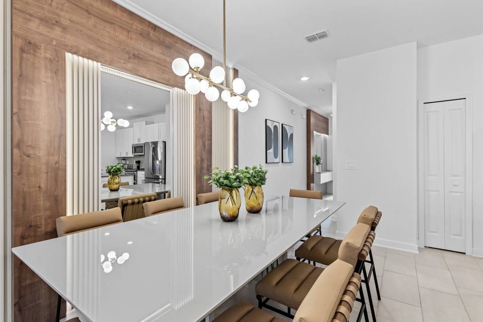 Enjoy meals and conversations at the sleek glass dining table, surrounded by stylish tan chairs. The warm wood accent wall and modern lighting create a bright, inviting atmosphere, enhancing your overall dining experience.