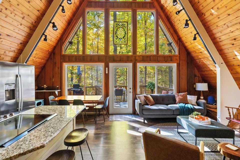 Open-Concept Kitchen/Dining/Living Area with Floor to Ceiling Windows that Frame a Stunning View of  the Surrounding Forest. 