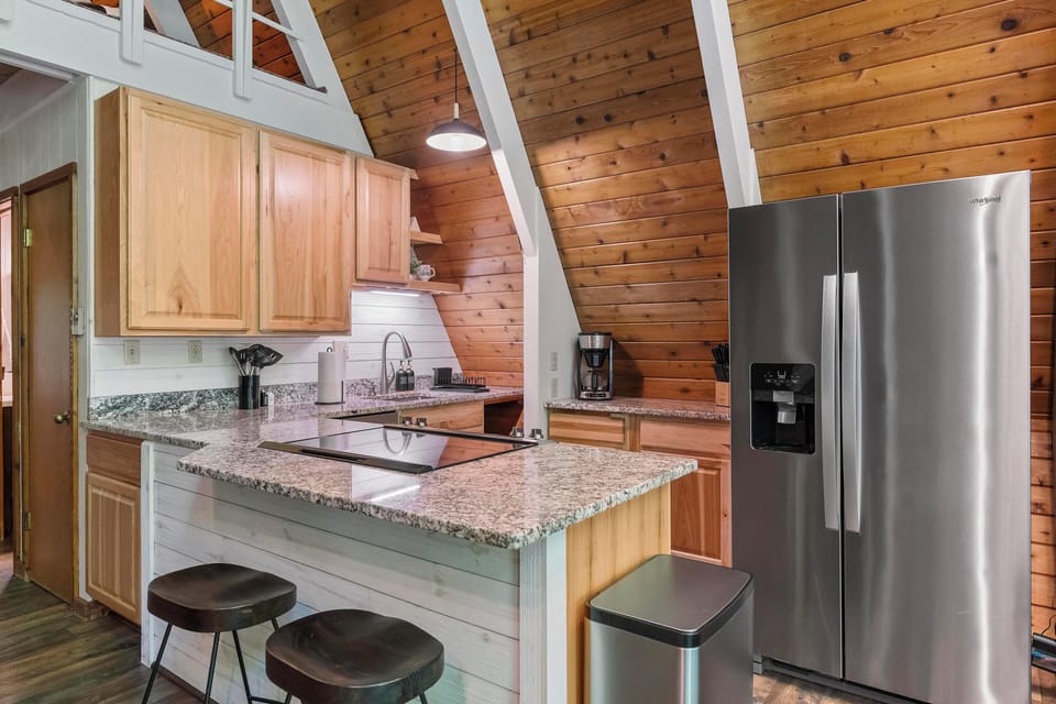 Fully equipped A-Frame kitchen with modern appliances, granite countertops, and cozy breakfast bar--perfect for cooking meals or enjoying coffee in a warm wood paneled setting. 
