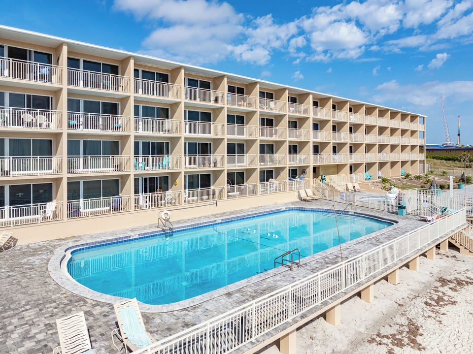 Resort-style building with a sparkling pool steps from the sand.