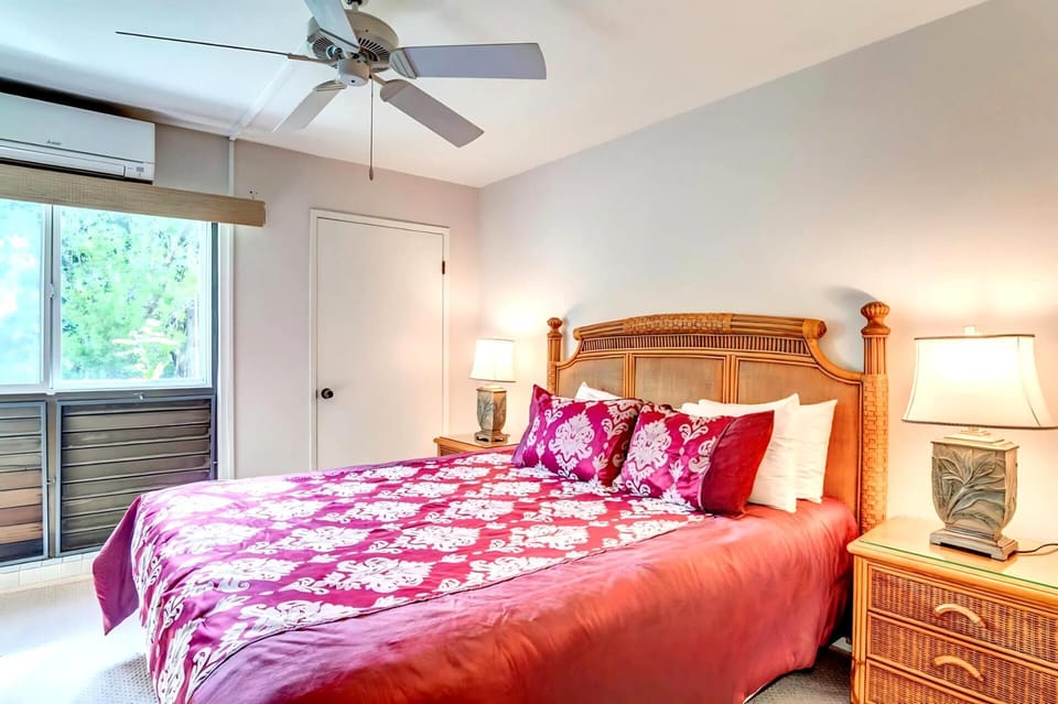 The master bedroom features a bold tropical bedspread, natural light streaming through the lanai doors, and a peaceful vacation ambiance. NAP-B43