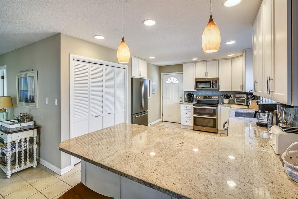 Picture yourself preparing morning coffee in this bright, fully-equipped kitchen with gleaming granite countertops, stainless steel appliances, and warm pendant lighting that makes every meal feel special.