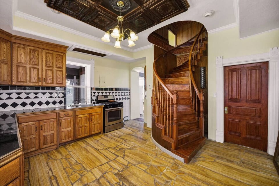 Brass candelabra light fixture overhead, dark embossed tin ceiling panels, solid oak cabinetry on every wall