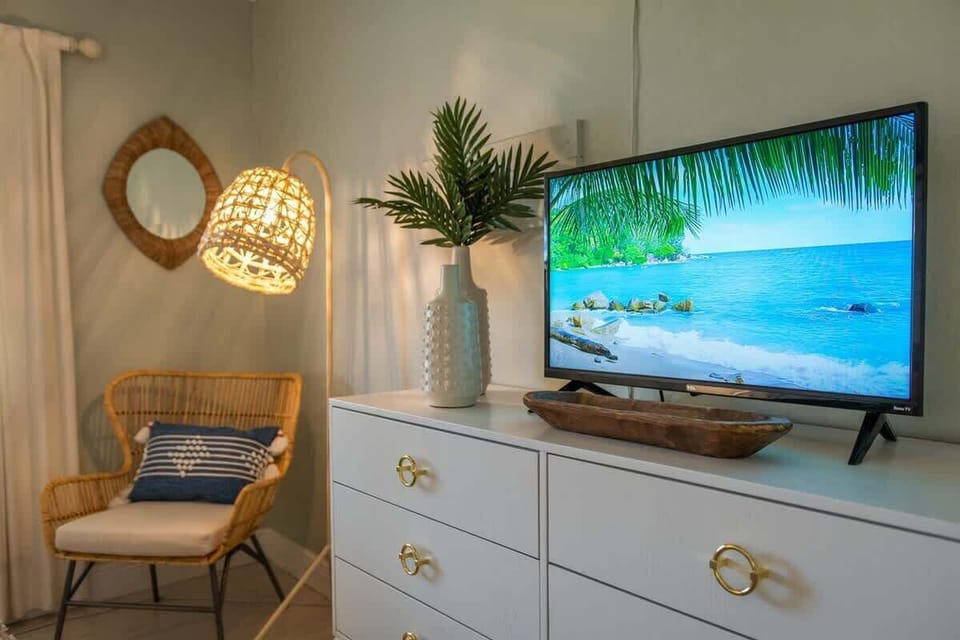 This bedroom features a king bed, dual nightstands with soft lighting, a dresser with a flat-screen TV, ceiling fan overhead, and a cozy reading nook.