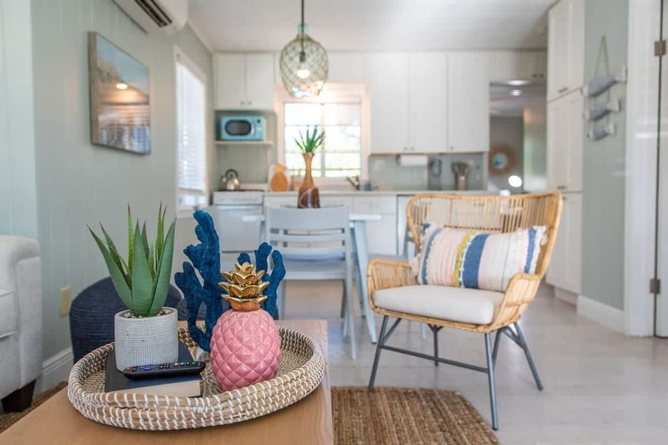 Living space features a plush sofa, accent chairs, TV, and a coffee table. The open layout connects to a kitchen with full appliances, dining table, and stylish pendant lighting.