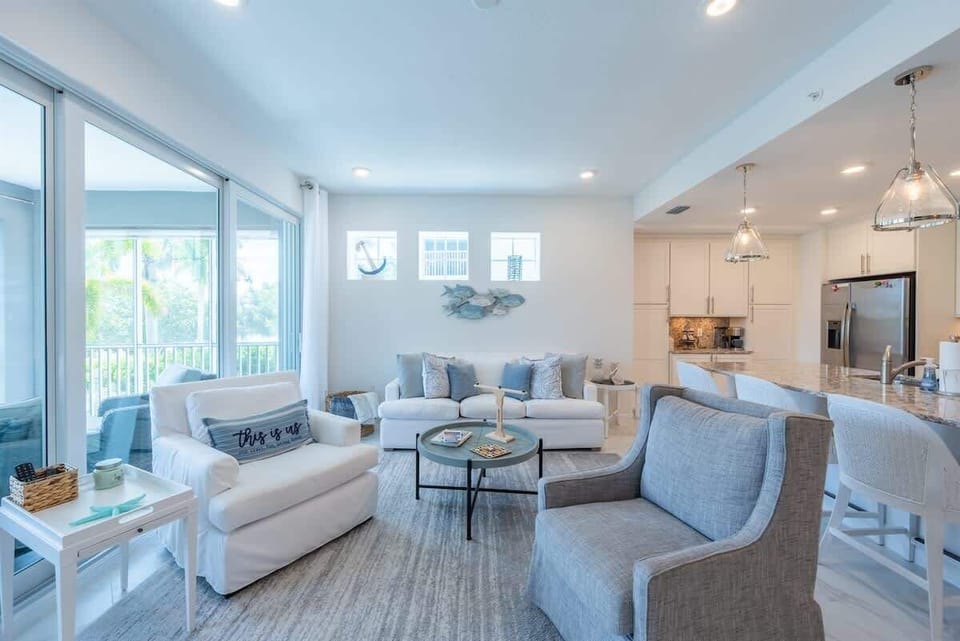 Living space with coastal décor, plush seating, smart TV, and sliding doors to a breezy porch. This open-concept room flows seamlessly into the kitchen and dining areas.