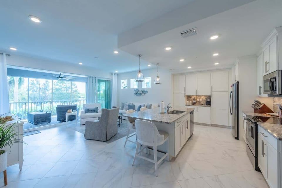 Living space with coastal décor, plush seating, smart TV, and sliding doors to a breezy porch. This open-concept room flows seamlessly into the kitchen and dining areas.