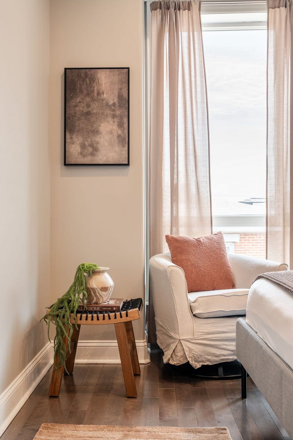 Cozy corner chair by a window with a wooden side table and soft lighting.