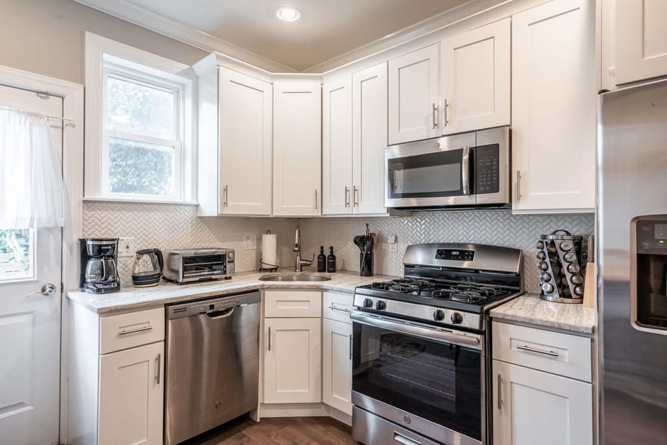 Sleek kitchen with white cabinets, steel appliance, and herringbone backsplash.