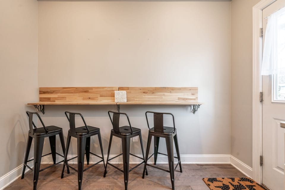 Narrow wooden bar with four black stools set against a minimalist wall.