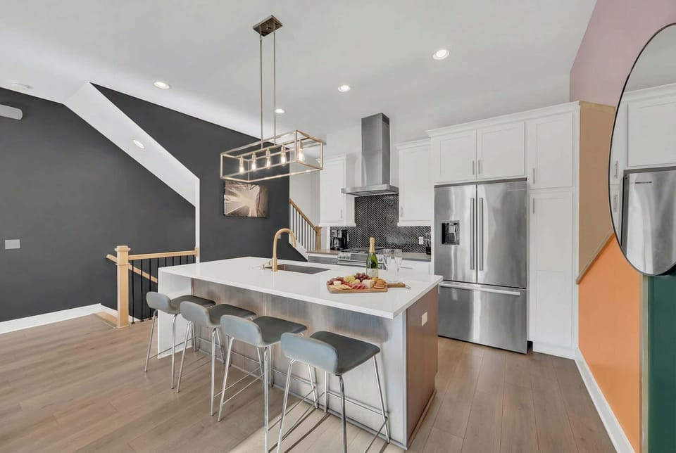 The kitchen anchors your crew around a generous island with bar stools, stainless steel finishes, and a dark accent wall that keeps everyone in the conversation while the cook works