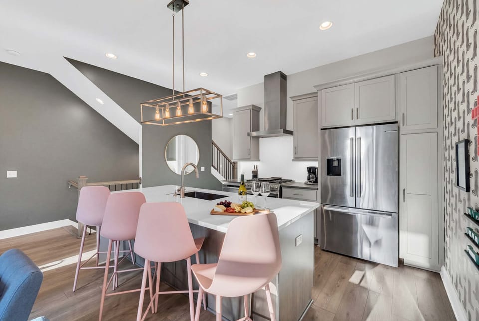 Kitchen island with pink bar stools and a sink in the center, stainless appliances flanking both sides, the real heart of group cooking and hangs