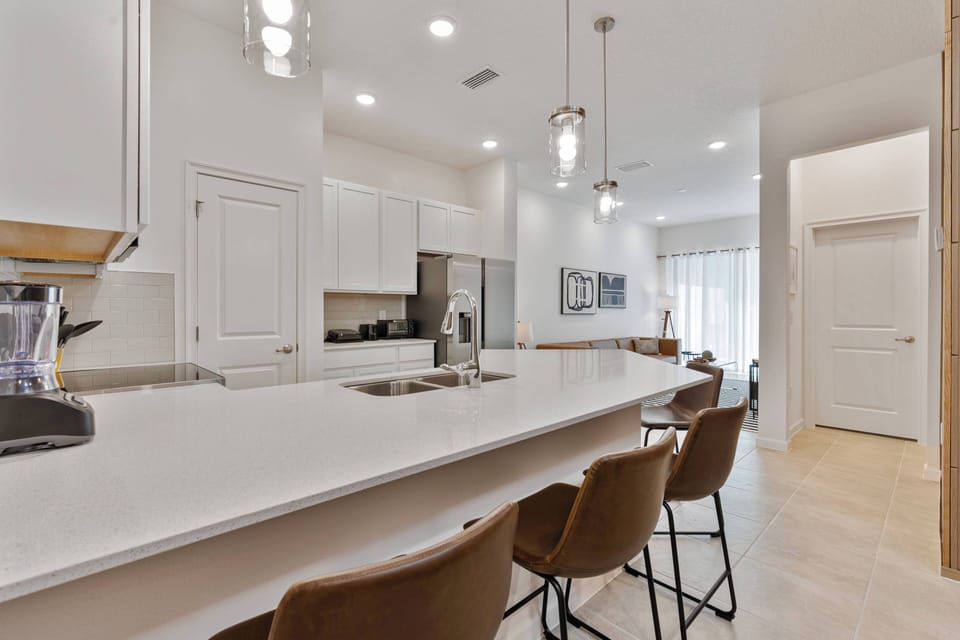 Step into this bright kitchen, where sleek white cabinetry pairs beautifully with a spacious quartz countertop. Enjoy the warm glow from pendant lights above the stylish bar seating, perfect for casual meals or morning coffee.