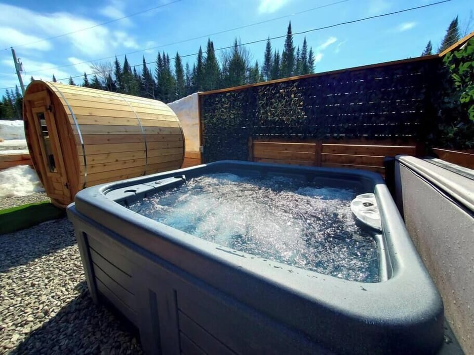 Votre retraite bien-être extérieure ultime : profitez d'un bain régénérant dans le bain à remous, suivi d'une séance détoxifiante dans notre sauna baril, le tout en pleine nature.