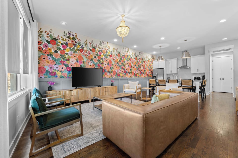 Located on the 2nd floor, the bright and stylish open-concept living room featuring comfortable seating, a large Smart TV, a colorful floral accent wall, and a vintage record player – perfect for relaxing and spending time together.