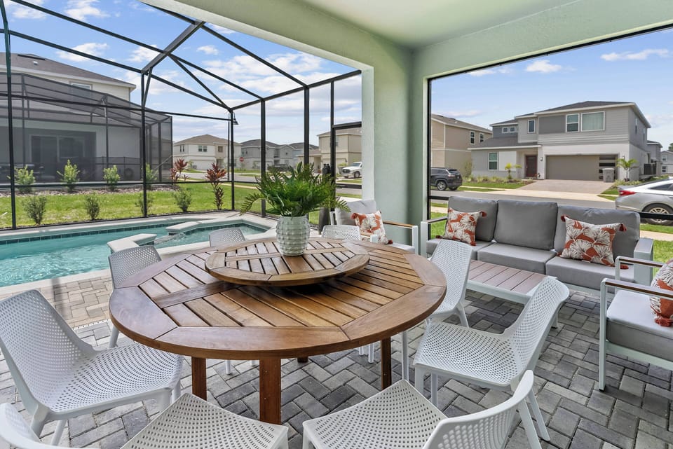 Experience the chic outdoor dining space with a round wooden table and sleek white chairs, ideal for al fresco meals. Large windows bring in natural light and showcase the stunning pool and lush greenery around you.